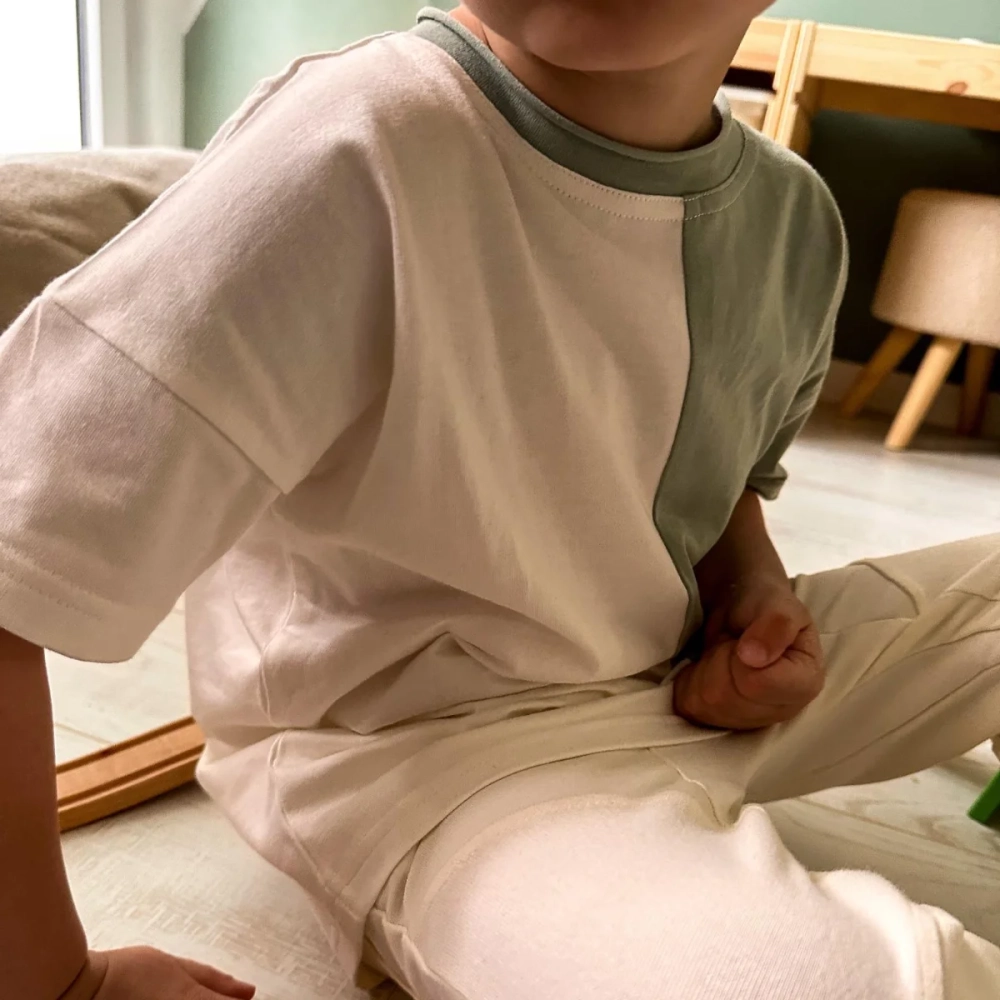 Zbliżenie na dziecko w dwukolorowym t-shircie Moss marki Buogo - kremowo-miętowym, które wygodnie siedzi na kanapie, pokazując detale miękkiego i przyjaznego materiału. Polska marka odzieży dziecięcej.