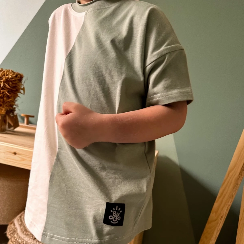 Dziecko nosi dwukolorowy t-shirt Moss w odcieniach kremowych i miętowych, prezentując wygodny krój i miękki materiał w przytulnym, domowym wnętrzu. Komfortowe ubrania dla dzieci Buogo.