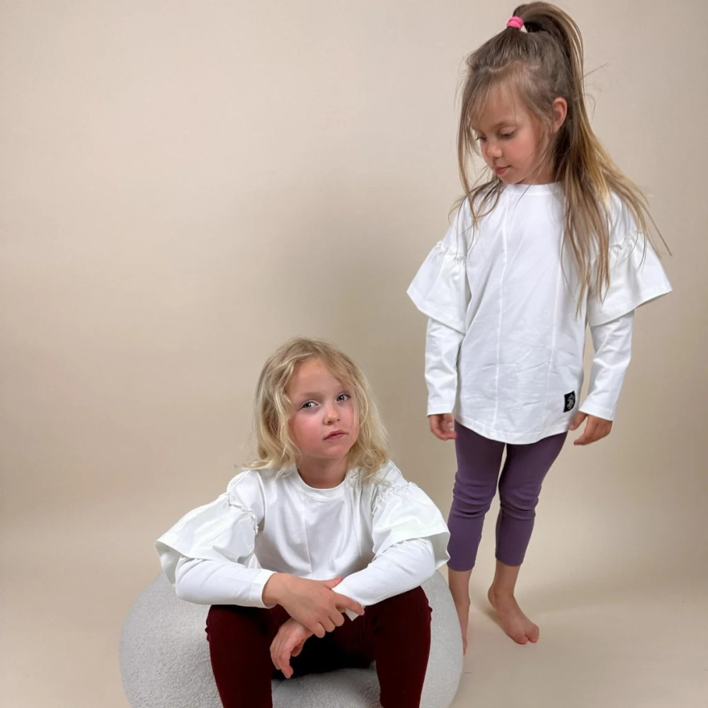Dwie dziewczynki w białych bluzkach Lily z ozdobnymi rękawami marki Buogo - moda dla dzieci