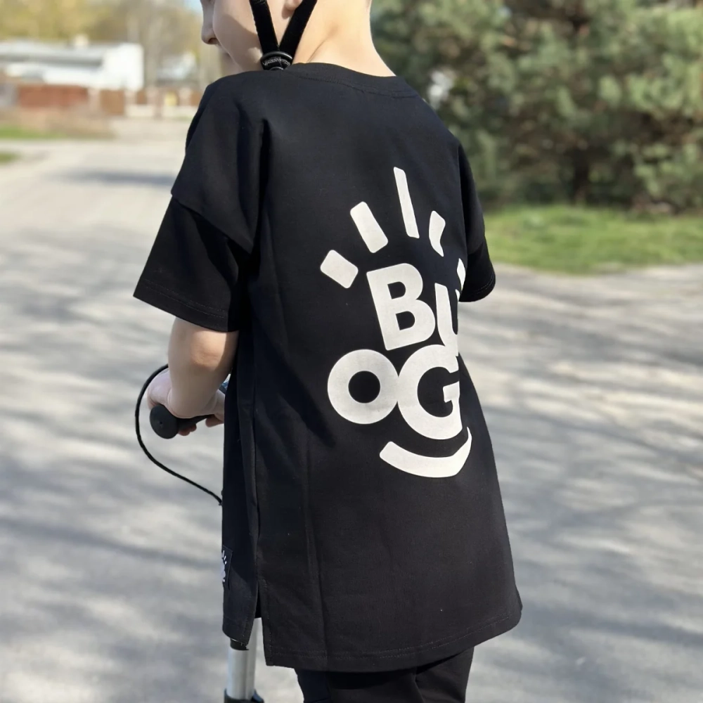 Chłopiec na rowerze ubrany w czarną koszulkę Daylight marki Buogo z wyrazistym białym logo na plecach – praktyczna i stylowa odzież dziecięca do codziennego użytku.